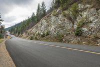 a motorcycle rides along a curved mountain road on a cloudy day, near the water