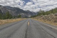 an empty road that goes out into the distance near a mountain range in the background