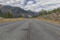 an empty road that goes out into the distance near a mountain range in the background