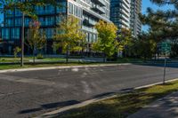 empty street in urban area with tall building in background against blue sky with trees and grass