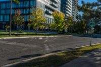 empty street in urban area with tall building in background against blue sky with trees and grass