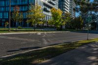 empty street in urban area with tall building in background against blue sky with trees and grass