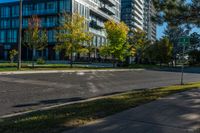 empty street in urban area with tall building in background against blue sky with trees and grass