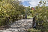 a wooden bridge over a paved path in the autumntime with fall foliage and a path winding through it