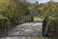 a wooden bridge over a paved path in the autumntime with fall foliage and a path winding through it