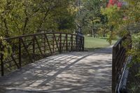 a wooden bridge over a paved path in the autumntime with fall foliage and a path winding through it