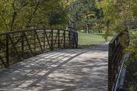 a wooden bridge over a paved path in the autumntime with fall foliage and a path winding through it