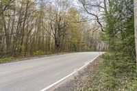 a motorcycle is driving down the road in front of some trees in the middle of a rural area