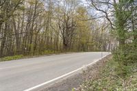 a motorcycle is driving down the road in front of some trees in the middle of a rural area