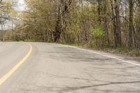 a road through the woods with some trees on both sides and an asphalt roadway and one with yellow and green lines