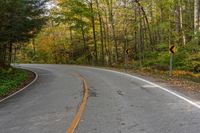 an empty road winding through woods in the fall leaves are changing colors while traffic signs line it