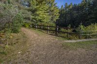 a trail leading up to an enclosed area in the woods of trees with a wooden fence