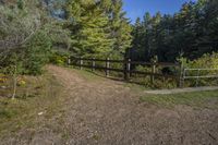 a trail leading up to an enclosed area in the woods of trees with a wooden fence