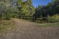 a trail leading up to an enclosed area in the woods of trees with a wooden fence