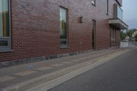 a side walk in front of a red brick building with a black door and windows