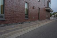 a side walk in front of a red brick building with a black door and windows