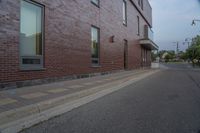 a side walk in front of a red brick building with a black door and windows