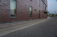 a side walk in front of a red brick building with a black door and windows