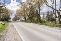 a person riding a bicycle on the street next to trees and grass with blue sky in background