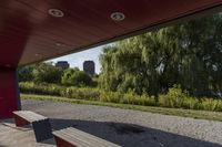 the view from behind a bench of a large city area next to a river, under which there are trees and bushes