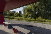 the view from behind a bench of a large city area next to a river, under which there are trees and bushes