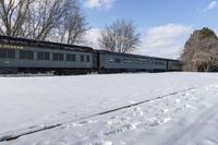 a train that is sitting in the snow on tracks in a field with snow covered ground