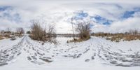 a winter landscape view of a lake and snowy field with footprints in the snow, taken through the fish eye lens lens