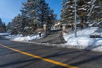 the road is covered with snow next to some trees and bushes for a driveway entrance