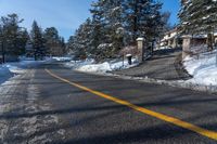 the road is covered with snow next to some trees and bushes for a driveway entrance