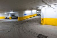 the empty parking area in a yellow and white building with some cars in it on the road