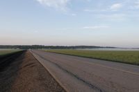 a car is driving down an open road next to the ocean and farmland in the distance