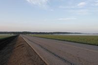 a car is driving down an open road next to the ocean and farmland in the distance