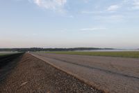 a car is driving down an open road next to the ocean and farmland in the distance