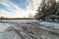 a small dirt patch with a sky filled with clouds and snow behind it with trees and power lines