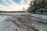 a small dirt patch with a sky filled with clouds and snow behind it with trees and power lines