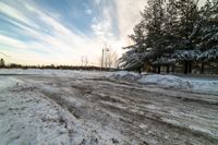 a small dirt patch with a sky filled with clouds and snow behind it with trees and power lines