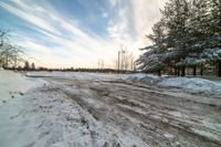 a small dirt patch with a sky filled with clouds and snow behind it with trees and power lines