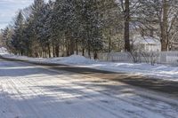 a snow covered street with a snowy fence in the distance and snow covered road leading the street