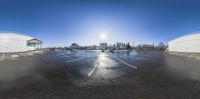 a wide angle lens shows cars passing in a parking lot on a sunny day with a bright sun overhead