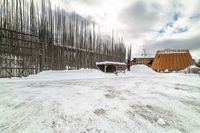 an empty wooden structure surrounded by snow on the ground and building in the background,