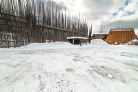 an empty wooden structure surrounded by snow on the ground and building in the background,