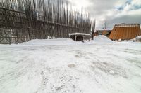 an empty wooden structure surrounded by snow on the ground and building in the background,