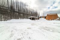 an empty wooden structure surrounded by snow on the ground and building in the background,