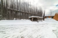 an empty wooden structure surrounded by snow on the ground and building in the background,