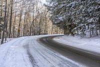 a curved road is bordered by trees on a snow covered mountain side and the road is very icy and snowy