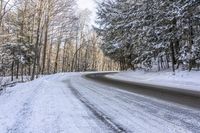 a curved road is bordered by trees on a snow covered mountain side and the road is very icy and snowy