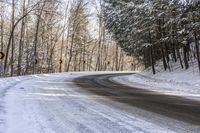 a curved road is bordered by trees on a snow covered mountain side and the road is very icy and snowy