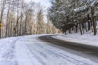 a curved road is bordered by trees on a snow covered mountain side and the road is very icy and snowy