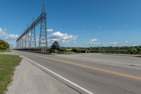 an empty highway under a power line under blue skies above the street and bushes of green