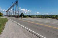 an empty highway under a power line under blue skies above the street and bushes of green